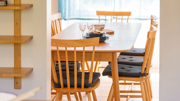 Un comedor con una mesa y sillas de madera, una pila de platos y un tazón.