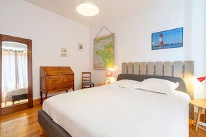 Un dormitorio con cama, cómoda de madera, mapa y un cuadro de un faro.