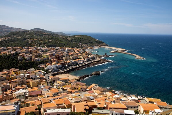 A coastal town with terracotta-roofed buildings, a marina, and a beach.