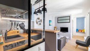 A modern kitchen with a built-in stove, a sink, and hanging utensils. There is a dining area with a table and chairs, a TV mounted on the wall, and a window with a view of the outside. - Bright 2-room apartment in Paris 1er near the Louvre and Notre-Dame (Paris)
