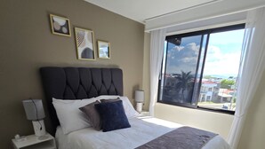 A bedroom with a large bed, a nightstand, a lamp, a window with a view, and a rug.