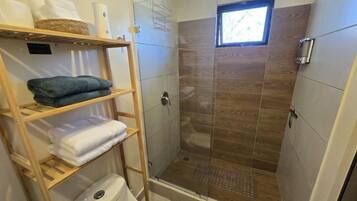 Ein Badezimmer mit Duschkabine aus Glas, Toilette und Ablagefläche für Handtücher.