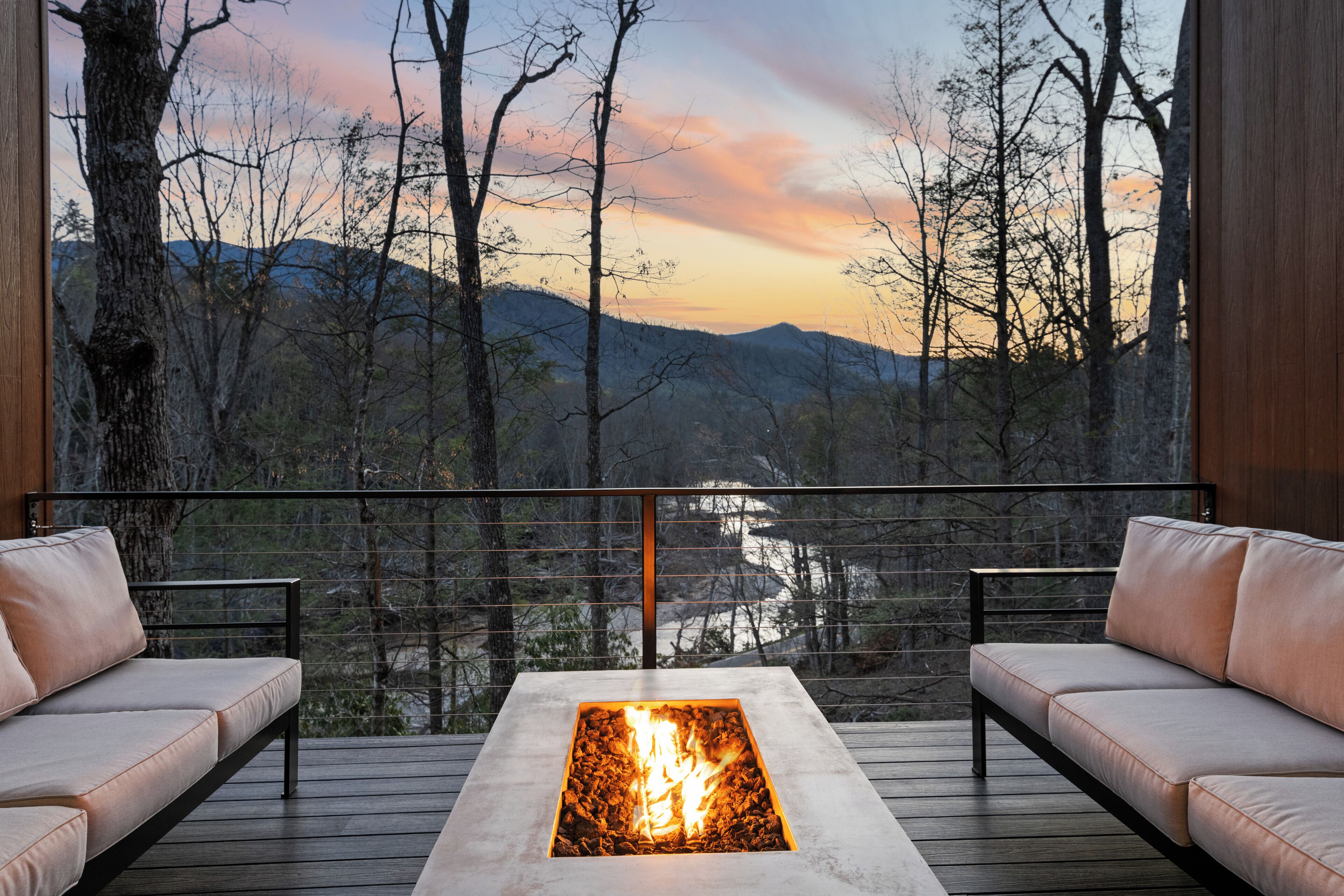 Une terrasse dotée d’un foyer extérieur, de deux canapés et offrant une vue sur une forêt et des montagnes.