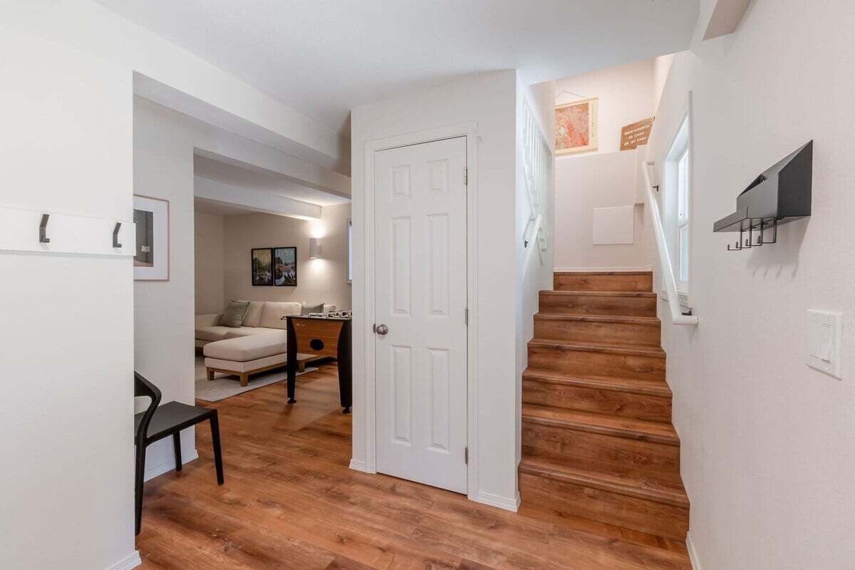 A hallway with a wooden staircase, a white door, and a seating area with a sofa and a table.