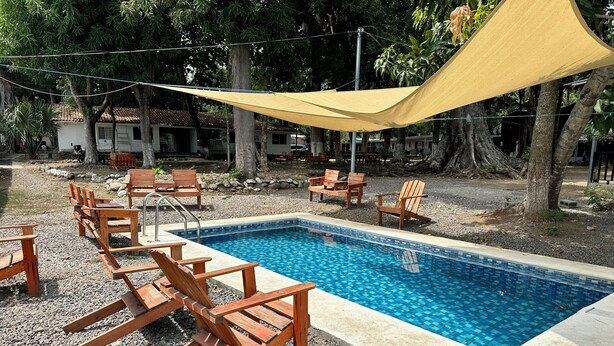 A swimming pool with wooden chairs and a shaded area.