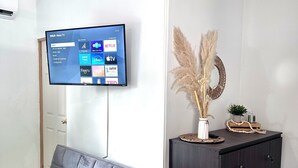 A modern living room with a grey sofa, a flat-screen TV mounted on the wall, and a dark wooden cabinet with decorative items.