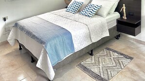 A bedroom with a bed, bedside tables, a hanging light fixture, a window, and a framed picture on the wall.