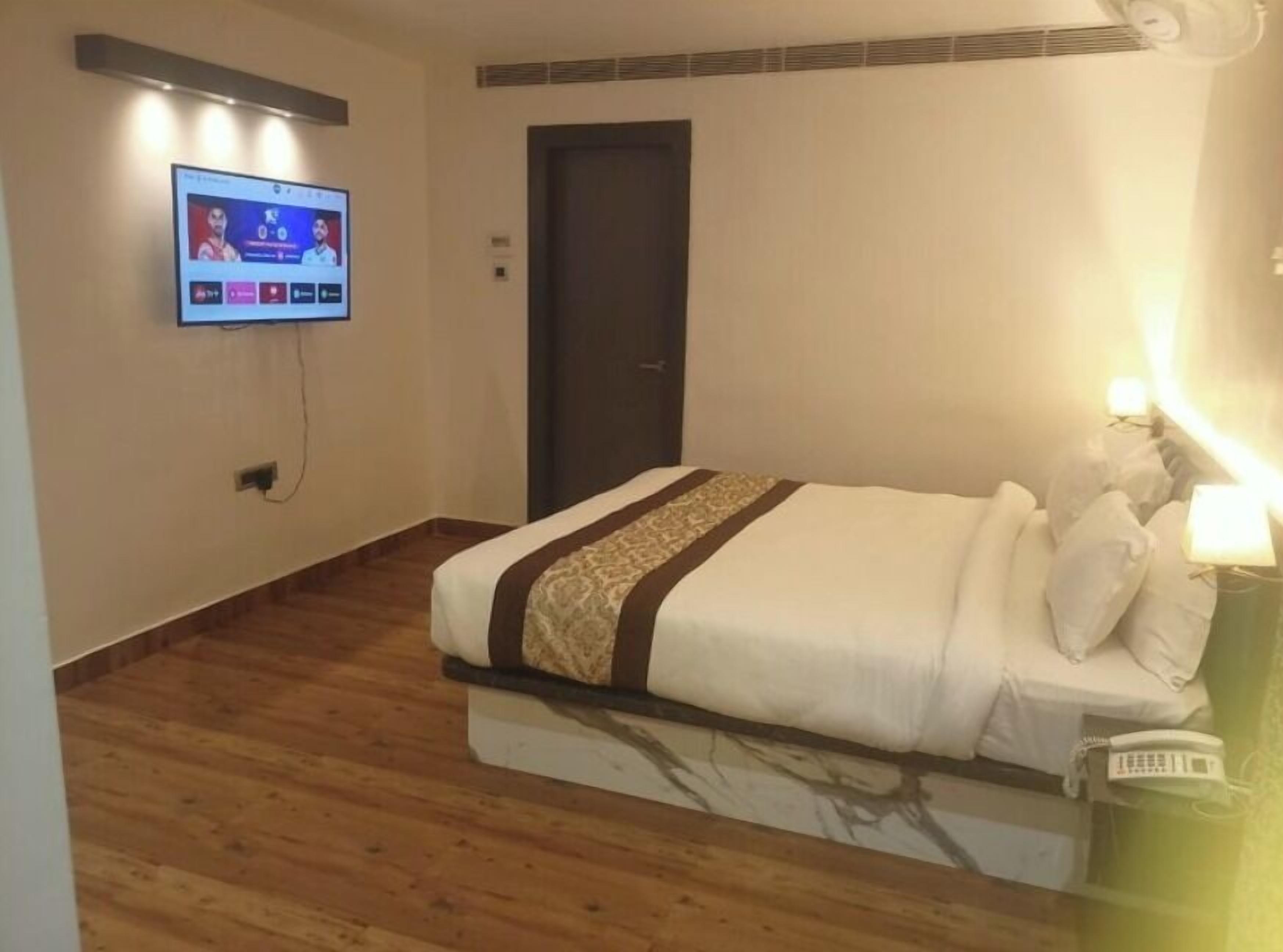 Quarto de hotel com uma cama, televisão fixada na parede e uma porta.