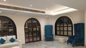 A modern living room with a white sofa, two blue armchairs, and a marble coffee table. - Hotel Golden Leaf (Ranchi)
