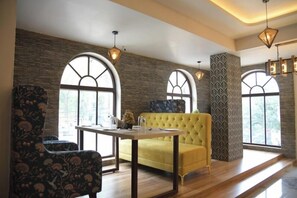 A room with a yellow sofa, a table, and a patterned armchair. There are large windows with arched tops and a brick wall. - Hotel Golden Leaf (Ranchi)