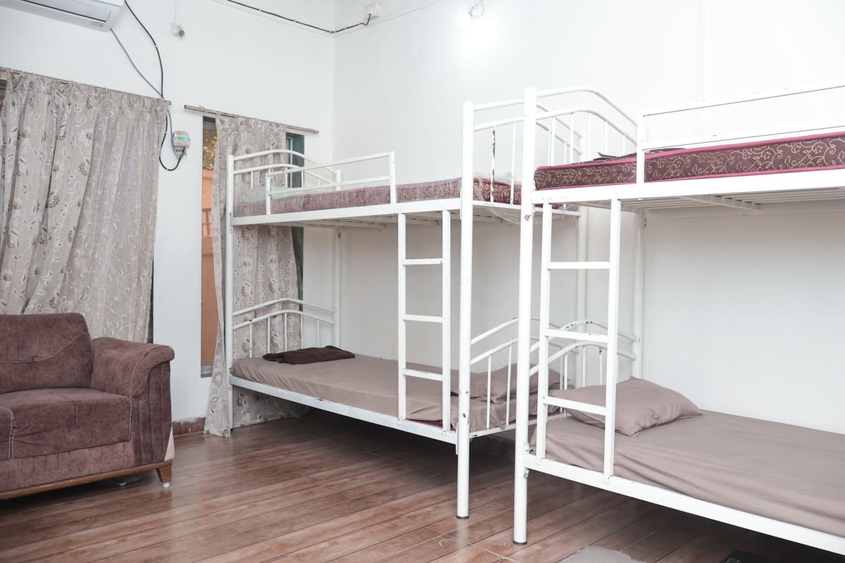 A dormitory room with bunk beds, a wooden floor, and a brown sofa.