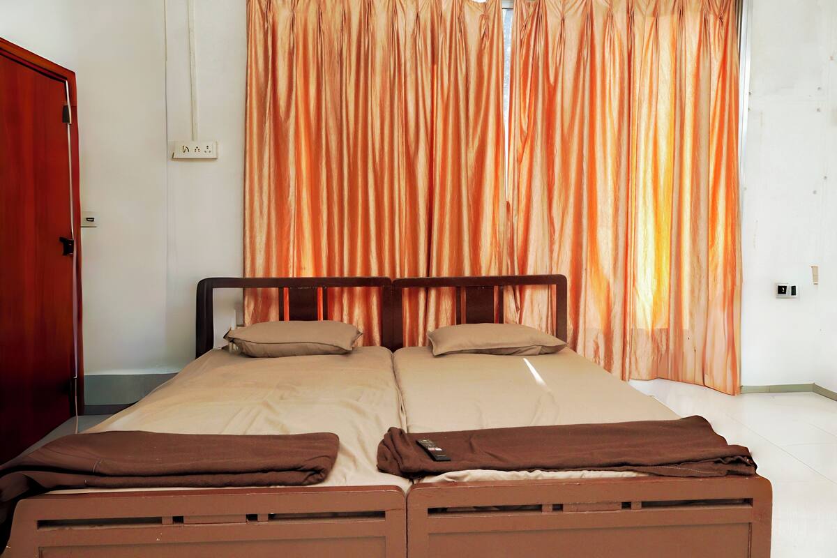 A double bed with two pillows and a blanket, a wooden headboard, and a curtain with vertical stripes.
