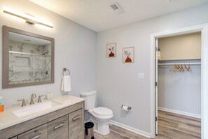 A bathroom with a marble sink, wooden vanity, white toilet, and a walk-in closet with wooden hangers. - Patio & Spacious Yard: Home in Athens (Athens)