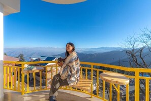 A person sitting on a yellow railing with a scenic mountain view in the background. - The Hosteller Narkanda (Kumharsain)