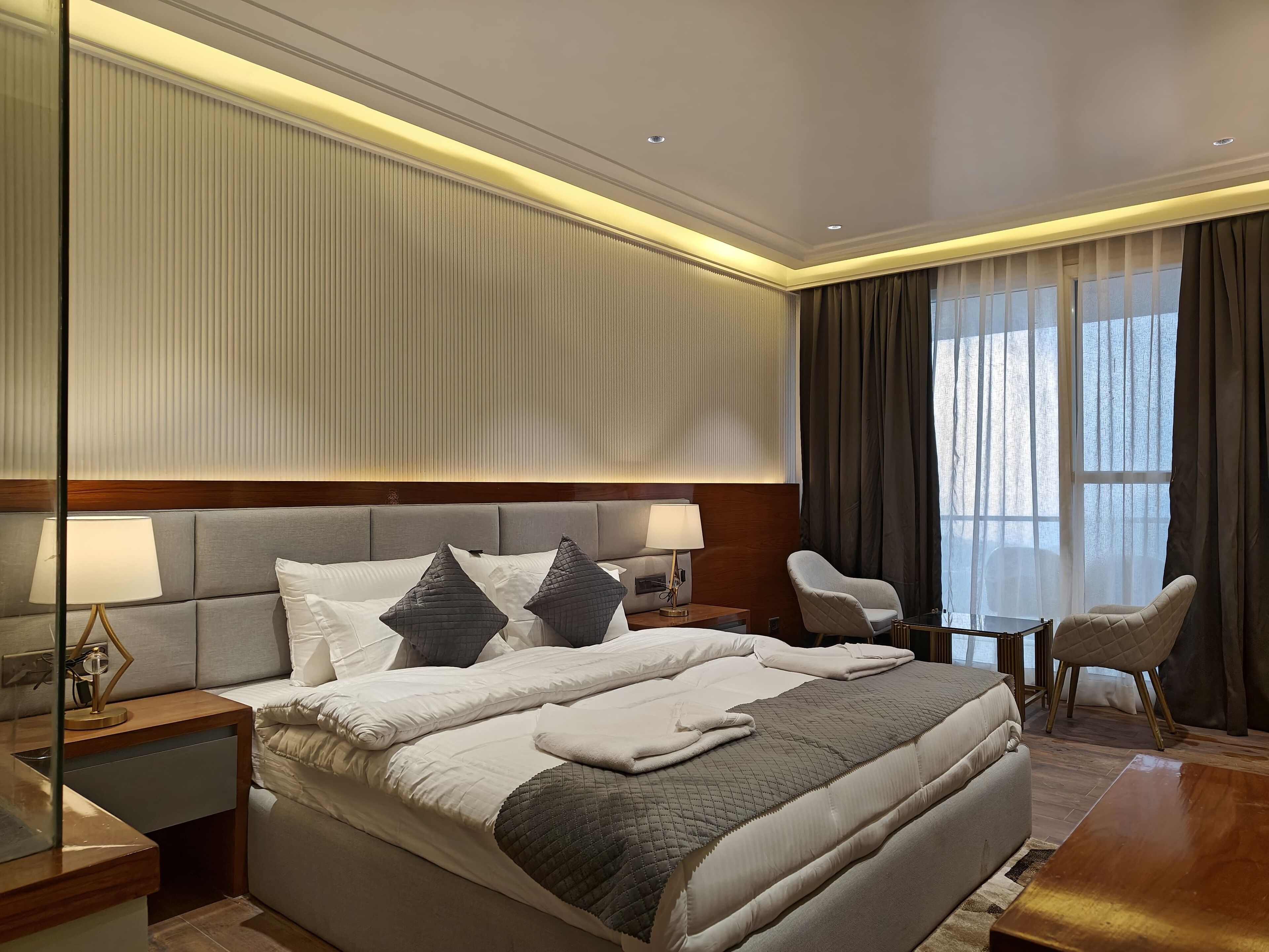 Una habitación de hotel con una cama grande, mesitas de noche, un escritorio y una silla.