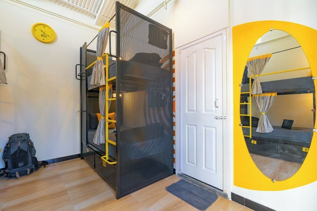 A room with a bunk bed, a door, a yellow circular mirror, a clock, and a small rug.