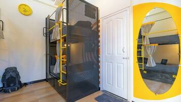 A room with a bunk bed, a door, a yellow circular mirror, a clock, and a small rug.
