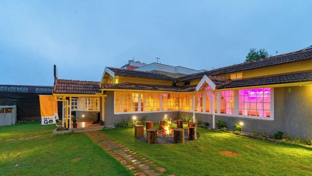 A two-story house with a well-maintained lawn and a fire pit in the center. - The Hosteller Ooty (Ootacamund)