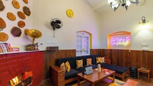 A cozy living room with a red brick fireplace, a black sofa with colorful cushions, a wooden coffee table, and a neon sign on the wall. - The Hosteller Ooty (Ootacamund)