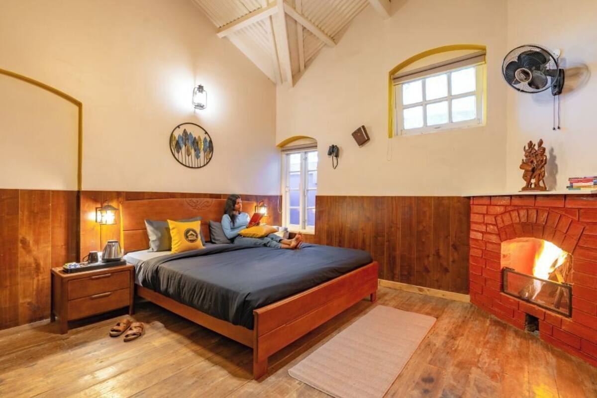 Ein Schlafzimmer mit einem hölzernen Bett, einem Nachttisch, einem Wandventilator, einem Kamin und einem Fenster mit Blick.