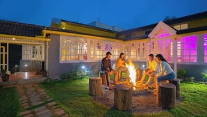 A courtyard with a fire pit, seating, and a building with large windows and a covered area. - The Hosteller Ooty (Ootacamund)