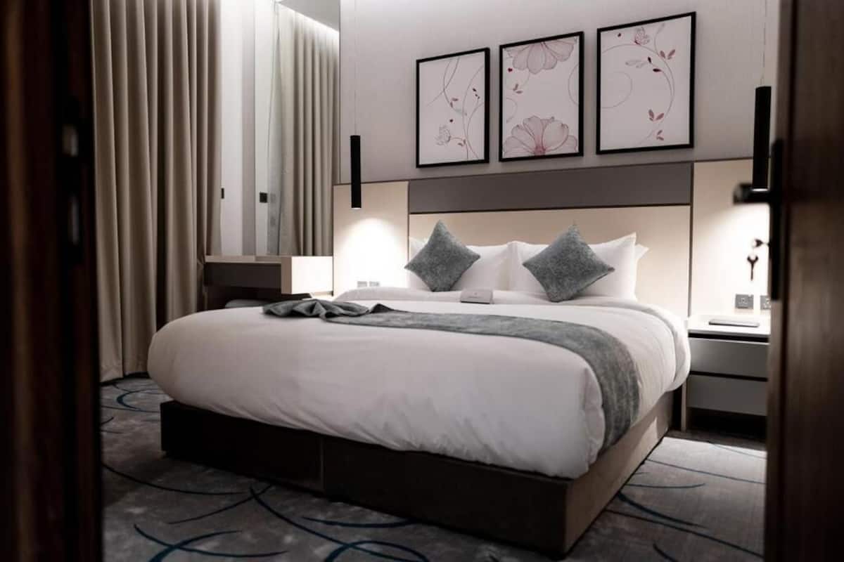 A modern hotel room with a large bed, bedside tables, and artwork on the wall.