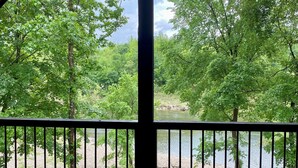A covered outdoor area with a wooden deck and a railing, overlooking a lake surrounded by trees. - RiverBend Haven-Sleeps 8-River Access (Broken Bow)