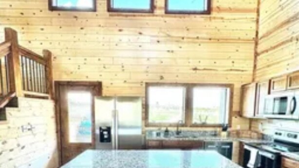 A wooden cabin interior with a kitchen area featuring a granite countertop, three stools, and a large window above the sink. - RiverBend Haven-Sleeps 8-River Access (Broken Bow)
