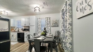 Una cocina moderna con armarios blancos, un refrigerador negro y una zona de comedor con una mesa dispuesta para cuatro.