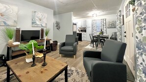 Una sala de estar con televisor, una mesa de centro de madera y un comedor con mesa y sillas.