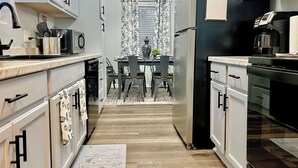 Una cocina moderna con armarios blancos, un refrigerador negro y un comedor con mesa y sillas.