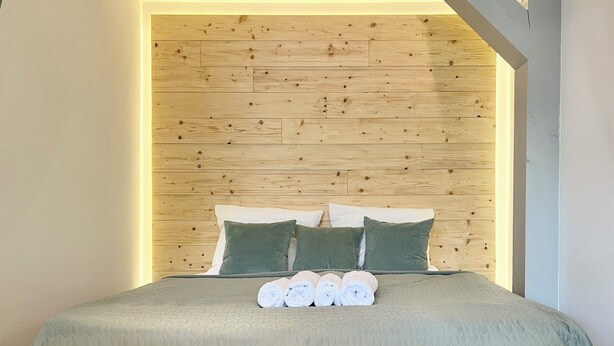 Un lit bien fait, avec une couverture verte et deux oreillers verts, une tête de lit en bois et un mur de couleur claire.