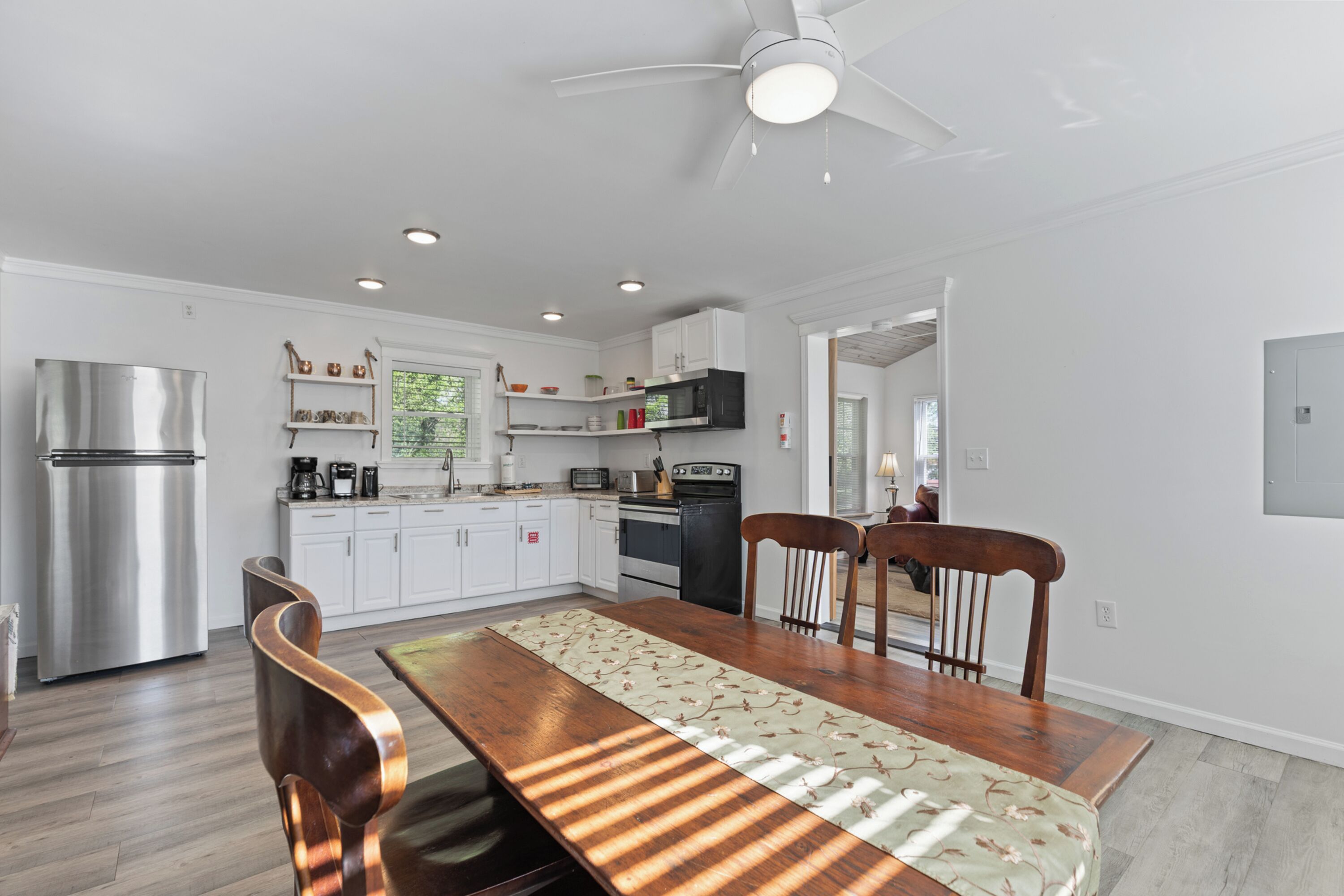 Una cocina moderna con armarios blancos, un refrigerador de acero inoxidable y un comedor con una mesa y sillas de madera.