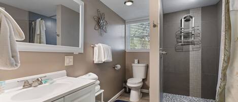 A bathroom with a white vanity, a large mirror, a shower with a glass door, and a blue bath mat.