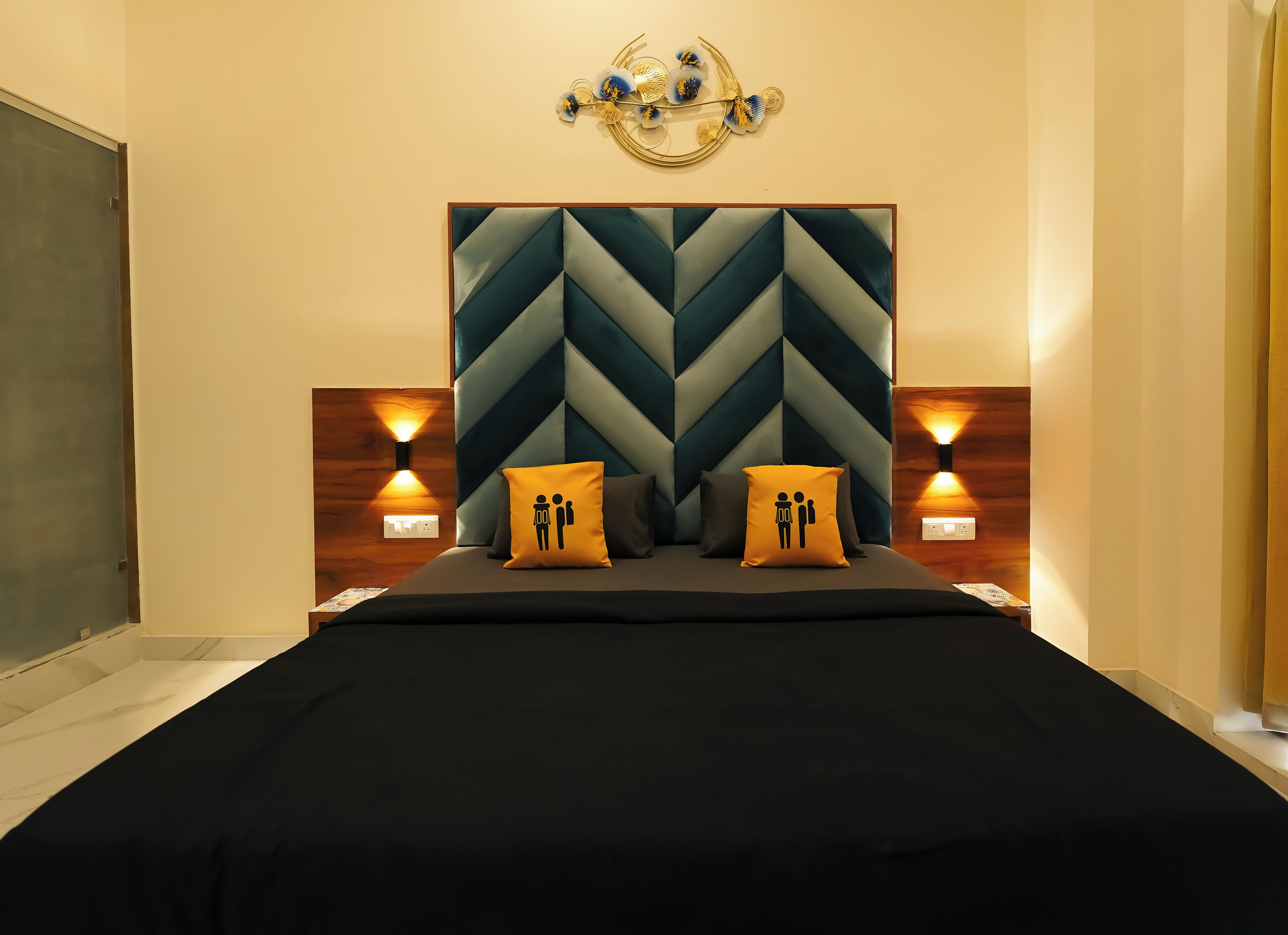 A modern bedroom with a geometric-patterned headboard, two bedside lamps, and two pillows with a male and female figure design.