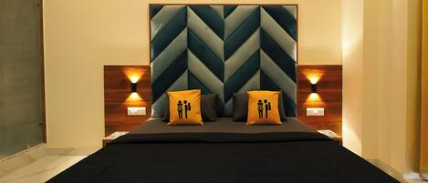 A modern bedroom with a geometric-patterned headboard, two bedside lamps, and two pillows with a male and female figure design.