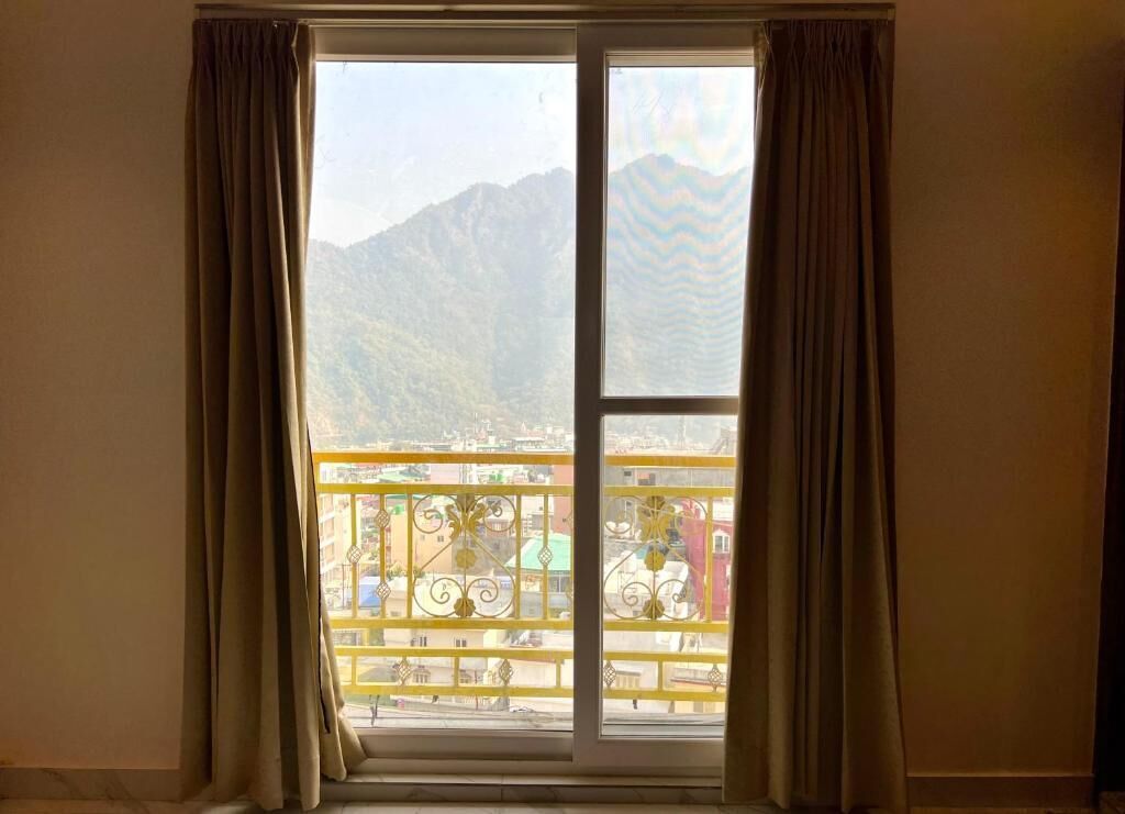 A room with a large window overlooking a balcony with yellow railings and a mountainous landscape in the background.