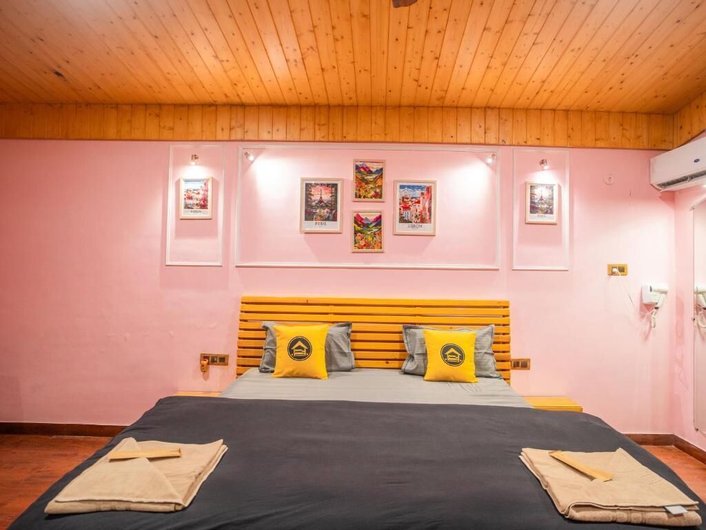 A bedroom with a wooden ceiling, a bed with a striped headboard, and four framed pictures on the wall.