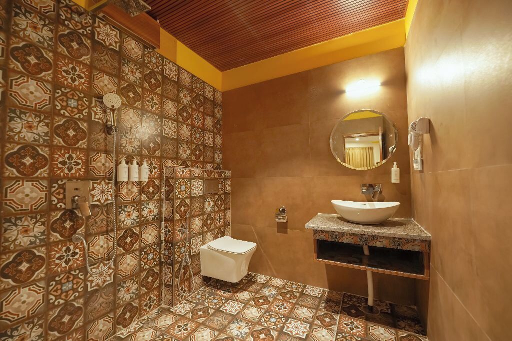 Ein Badezimmer mit gemusterten Fliesen, einem weißen Waschbecken, einem Spiegel und einer Dusche.