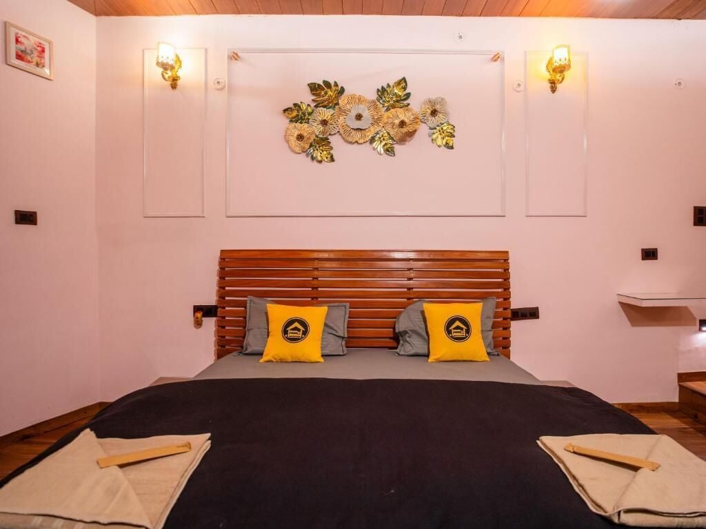 Une chambre à coucher avec une tête de lit en bois, deux oreillers ornés d’un logo, un élément décoratif mural et deux lampes fixées au mur.