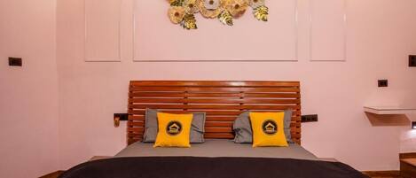 Un dormitorio con cabecera de madera, dos almohadas con un logotipo, un adorno de pared y dos luces fijadas a la pared.