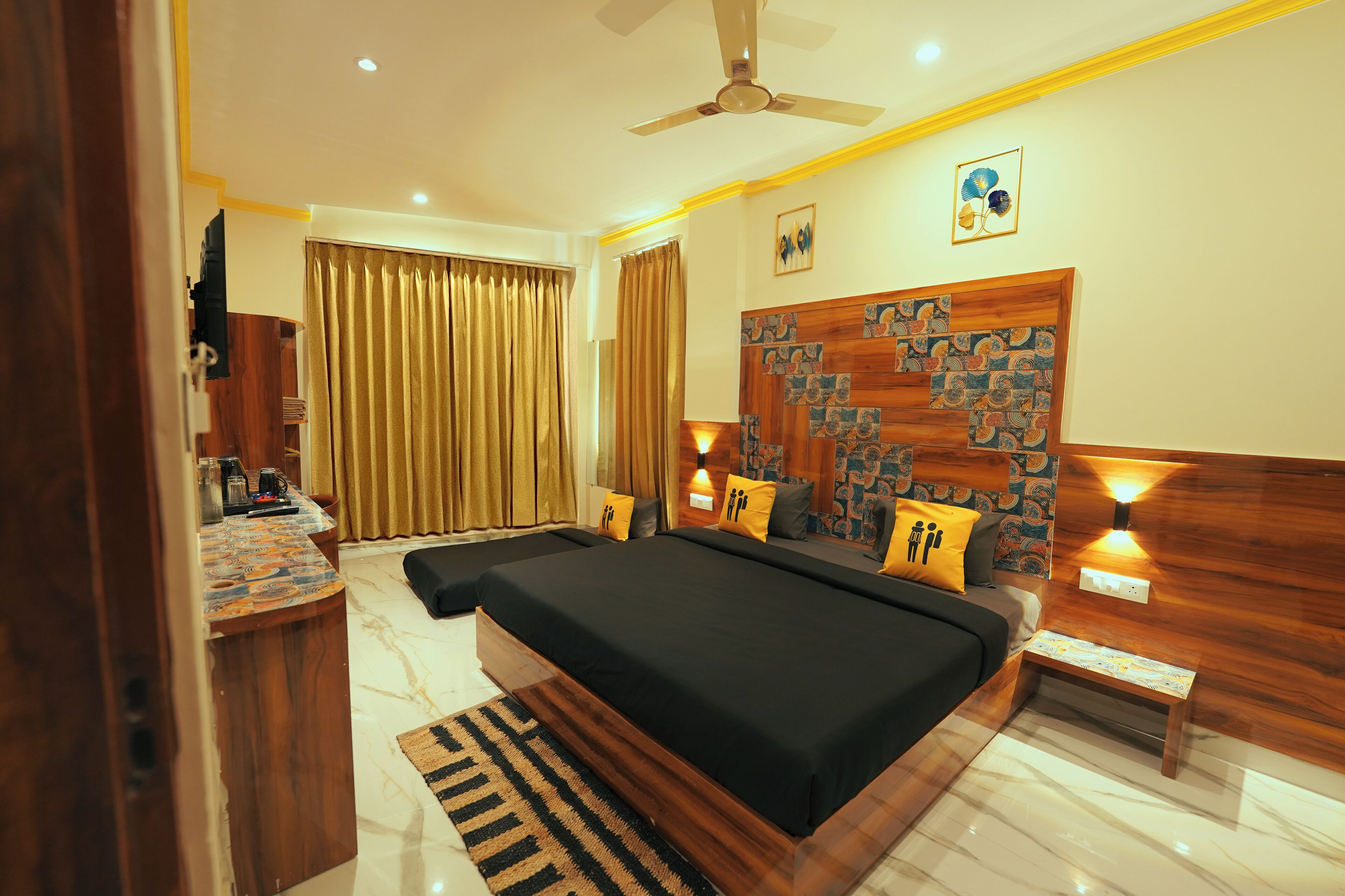 A hotel room with a large bed, a desk with a chair, a small table, and a ceiling fan.