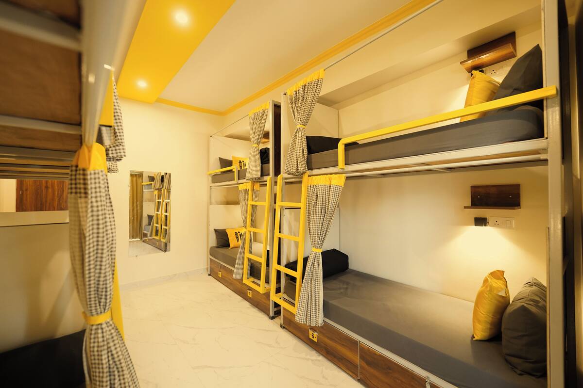 A bunk bed room with checkered curtains, a ladder, and a small shelf with a pillow.