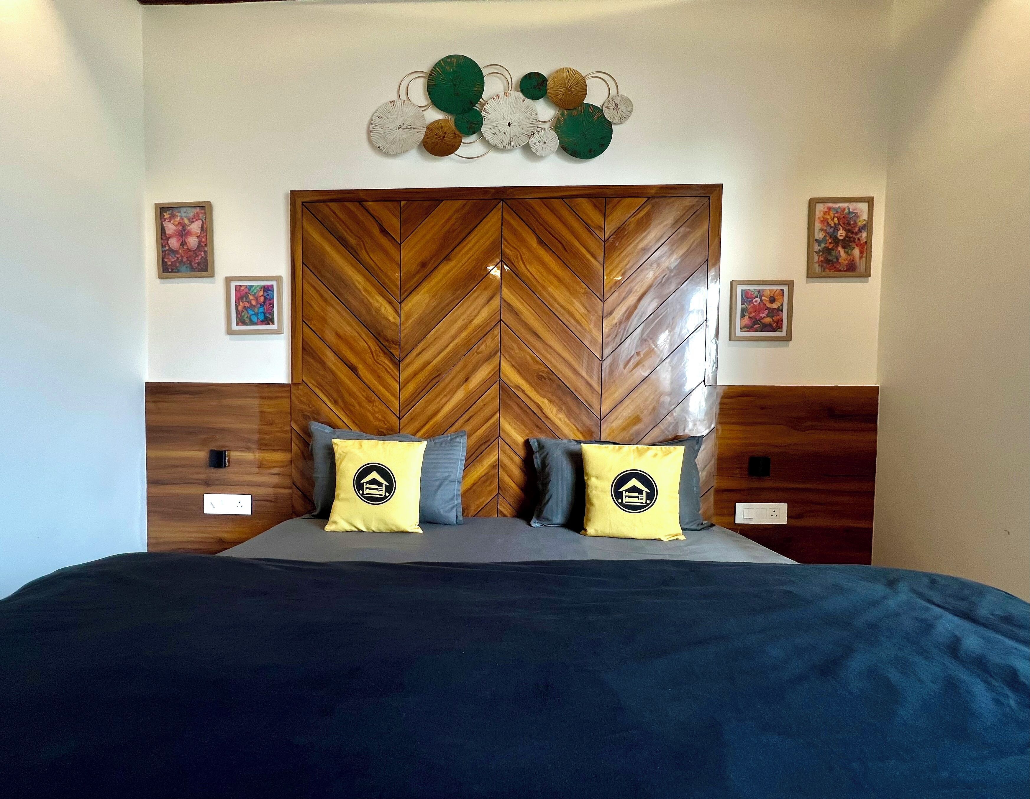 A bedroom with a herringbone-patterned headboard, two bedside tables, a bed with a dark blue bedspread, and two pillows with a house logo.