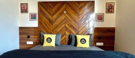 A bedroom with a herringbone-patterned headboard, two bedside tables, a bed with a dark blue bedspread, and two pillows with a house logo.