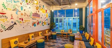 A cozy cafe with colorful murals, wooden furniture, and large windows offering a view of the cityscape.