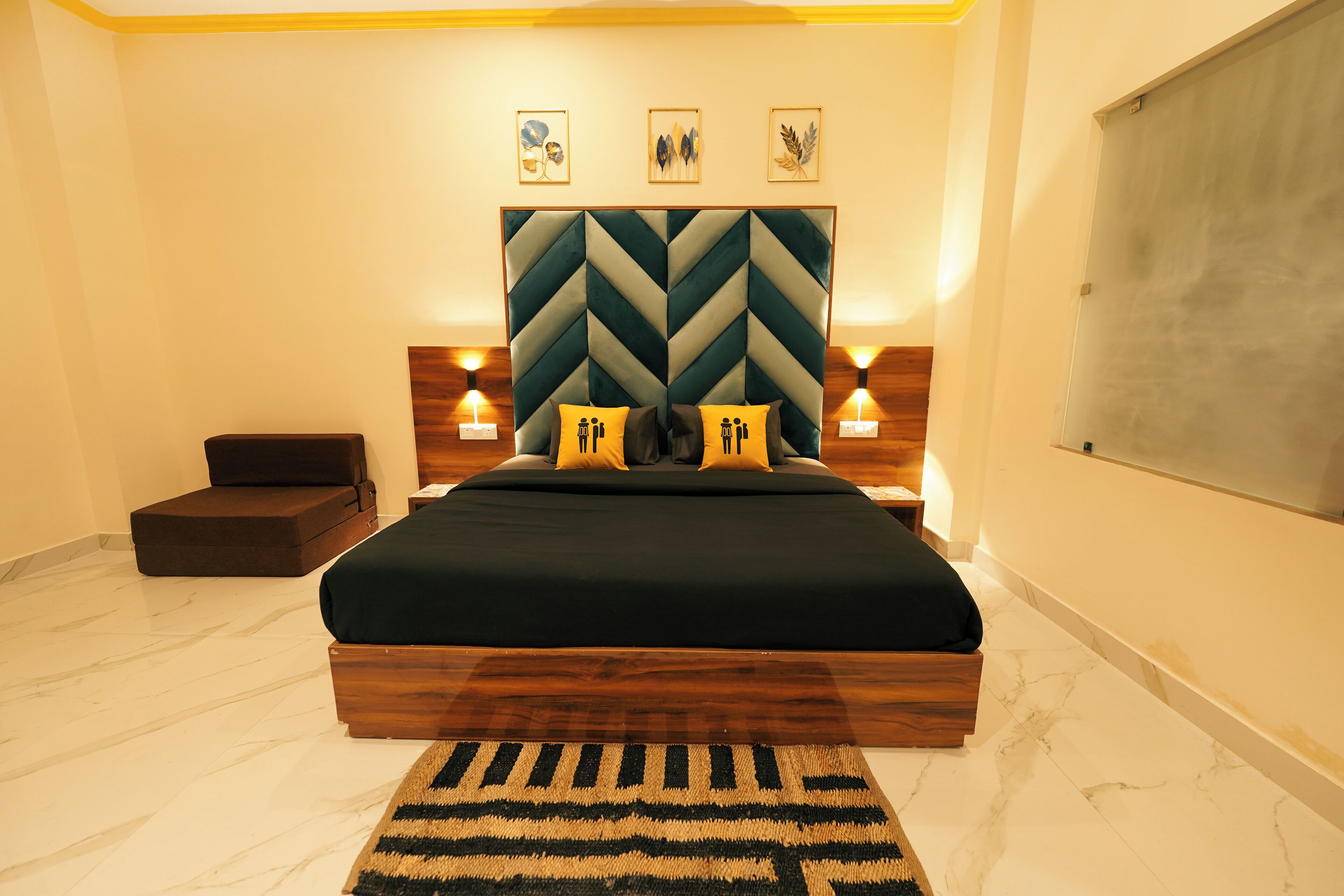 A modern bedroom with a large bed, wooden headboard, two bedside tables with lamps, a small bench, and a large window.