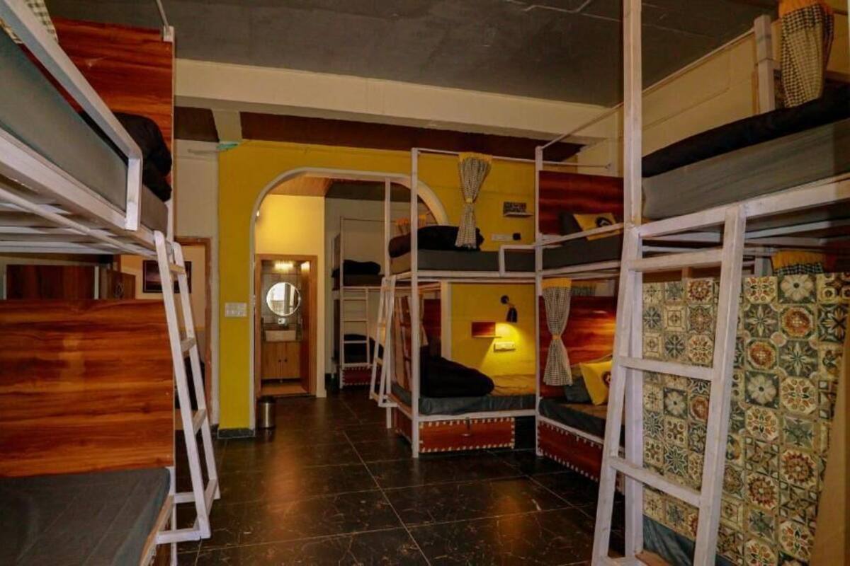A dormitory room with bunk beds, a small kitchenette, and a patterned wall.
