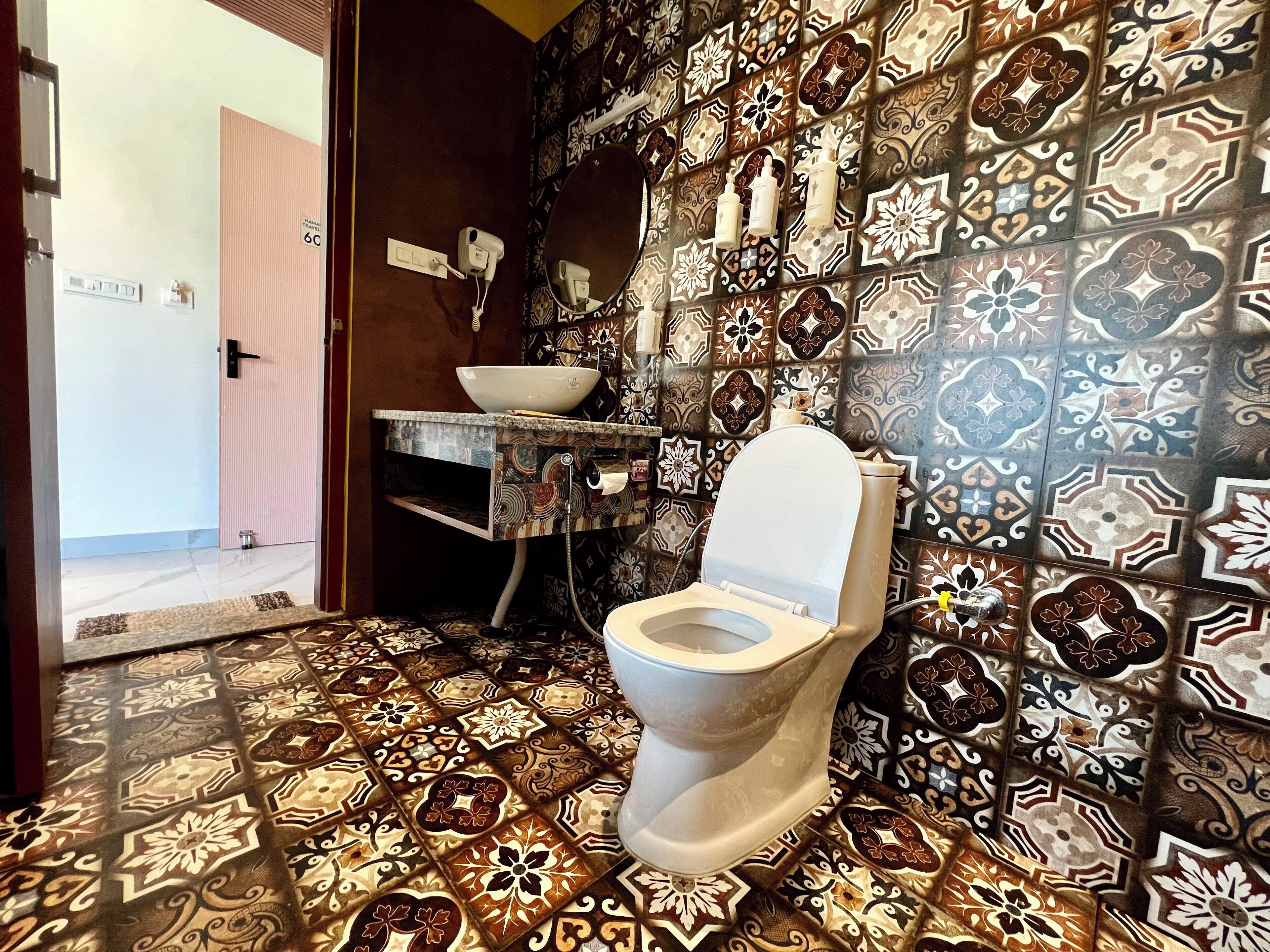 A bathroom with a patterned floor, a toilet, a sink with a mirror, and a wall-mounted hairdryer.