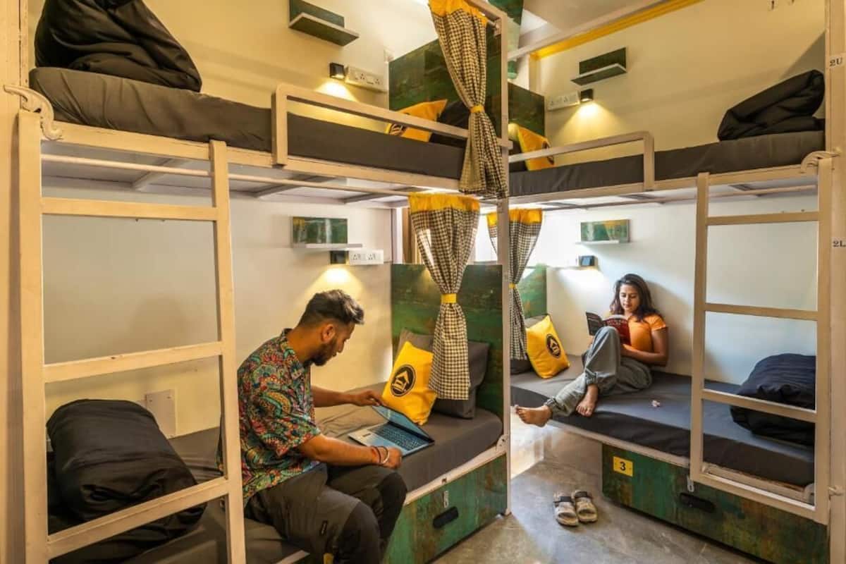 A dormitory room with bunk beds, a laptop on one bed, and a person reading on another.